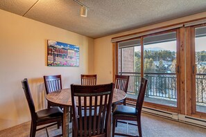 Un comedor con una mesa redonda y seis sillas de madera, un cuadro en la pared y un ventanal con vistas a un paisaje nevado.