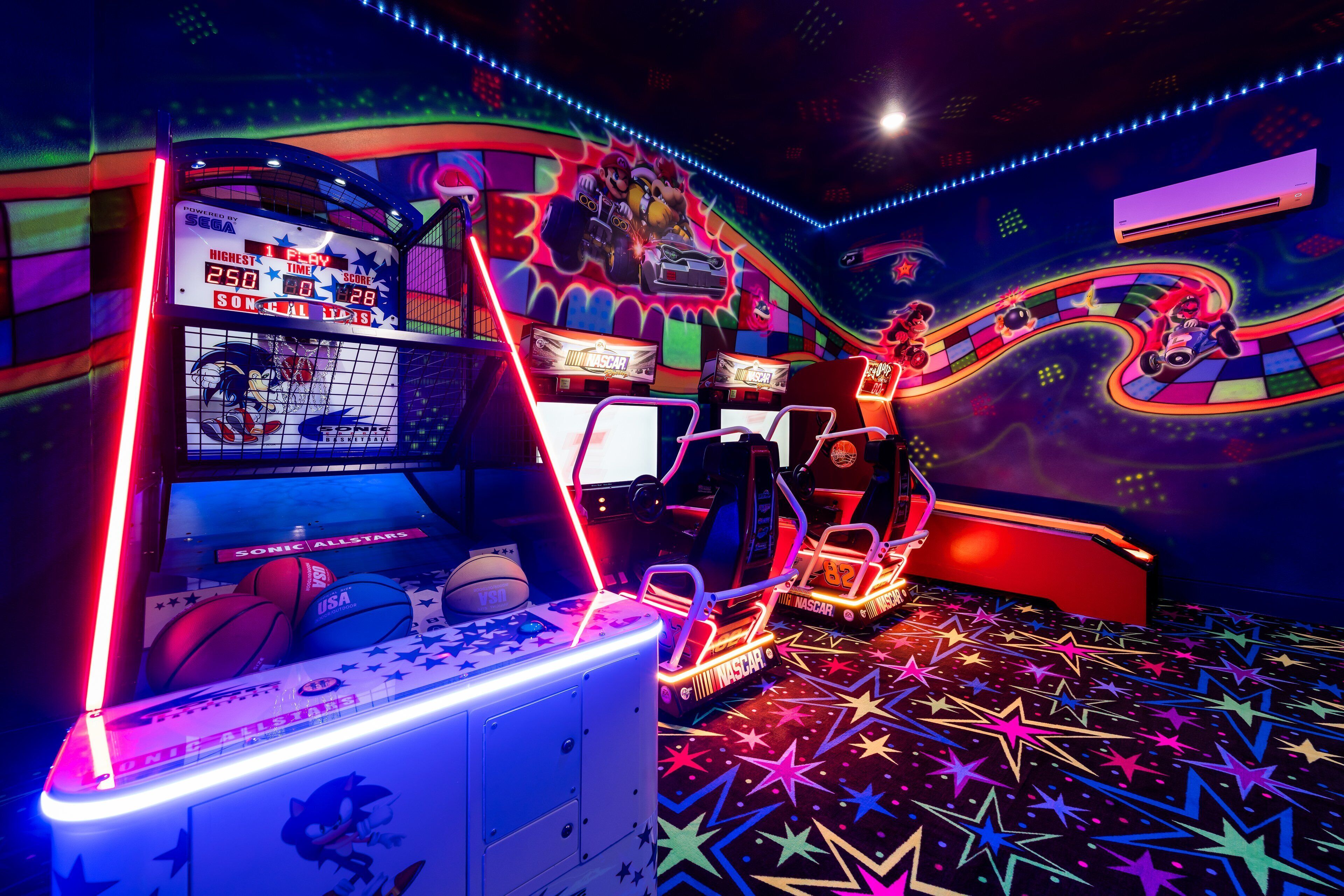 A brightly lit arcade room with racing game machines, neon lights, and a colorful floor design.
