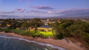 Una propietat a la costa amb platja, una casa ben il·luminada i una vista de la ciutat a la llunyania.
