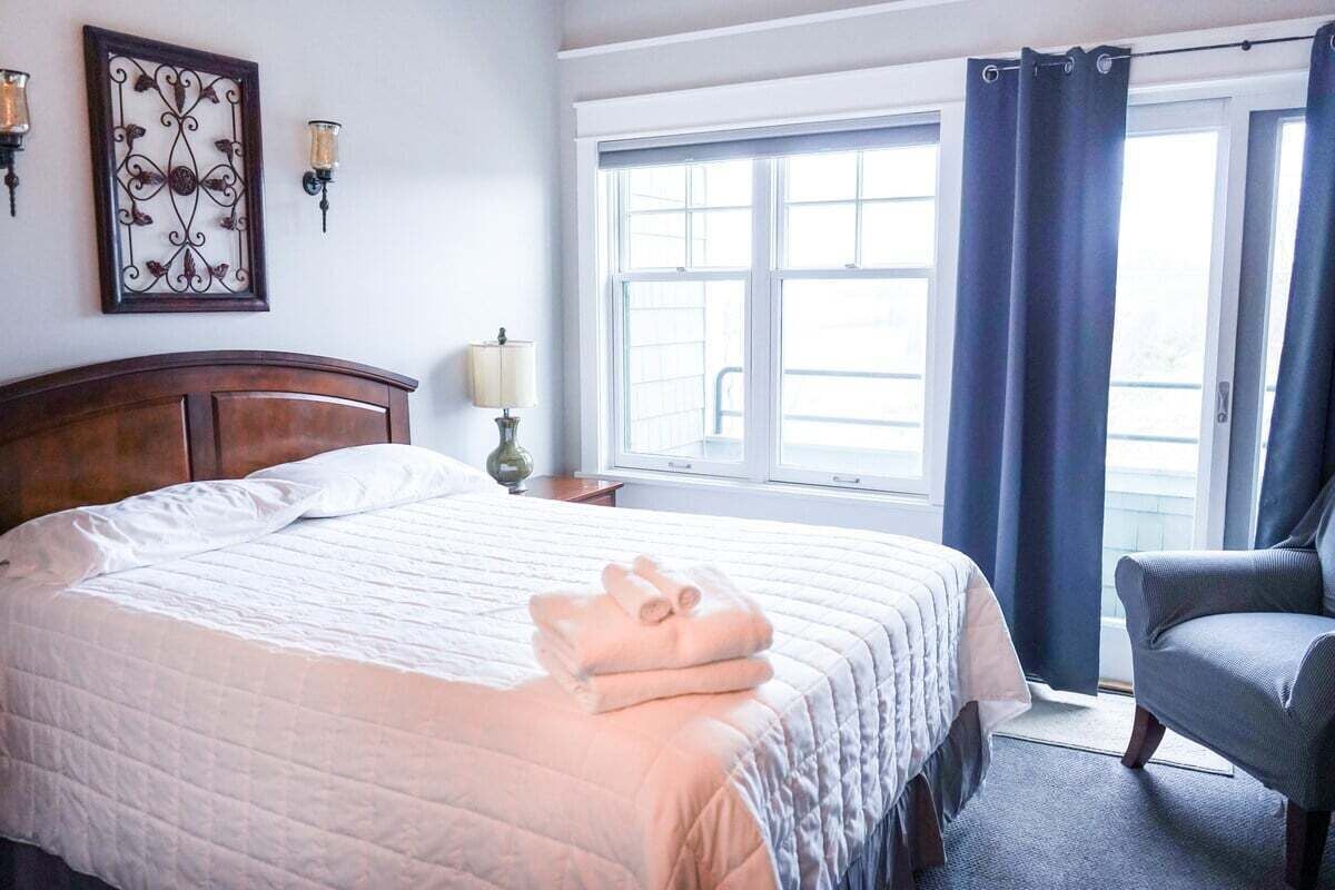 A hotel room with a large bed, a chair, a window with curtains, and wall sconces.