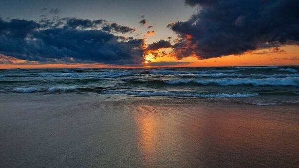 Uma praia com ondas e um pôr do sol.