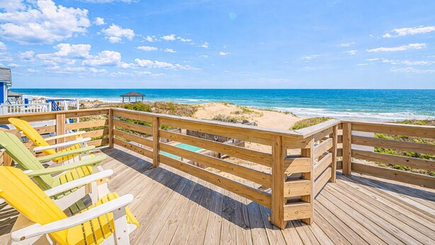 Una terraza de madera con sillas de playa con vista al océano.
