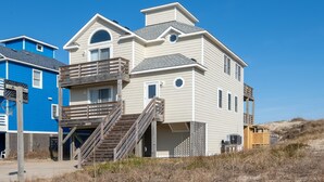 Una casa de playa de dos pisos con un balcón, una escalera y una pequeña terraza.