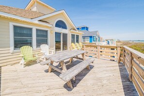 Eine Holzterrasse mit Picknicktisch und Stühlen mit Blick auf einen Strand.