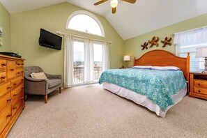 Ein Schlafzimmer mit Bett, Kommode, Stuhl, Fernseher und einem Fenster mit Vorhängen.