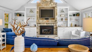 A spacious living room with a stone fireplace, a large flat-screen TV, and a blue sofa. - Walk to Beach and Town, Hot tub, Sleeps 8, Pet Friendly (Chatham)