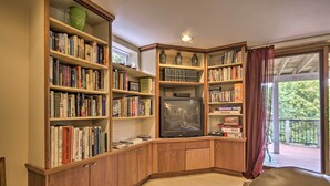 A corner room with wooden bookshelves filled with books, a television, and a window with a view of greenery.