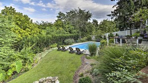 A backyard with a swimming pool, surrounded by lush greenery and a patio area with outdoor furniture.