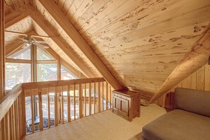 Ein Holzinnenraum mit schrägverdeckter Decke, einem Deckenventilator und Blick durch ein Fenster.