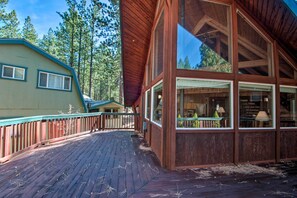 Una cabaña de madera con ventanas amplias, una terraza y vistas a los árboles circundantes.