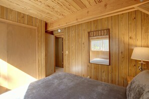 Une pièce aux murs lambrissés, avec un lit, une porte et une fenêtre.