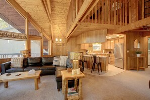 Un vaste espace de vie comprenant un canapé en cuir noir, une table basse en bois et une cuisine équipée d’un réfrigérateur et de meubles de rangement en bois.