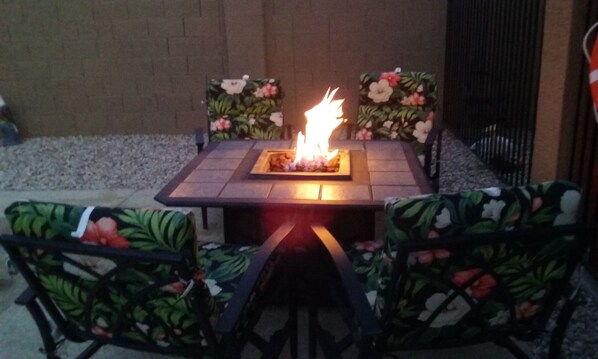 A square outdoor seating area with a central fire feature, surrounded by chairs with floral upholstery.