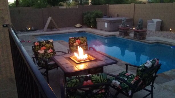 Una zona junto a la piscina con una mesa y chimenea, sillas y una pequeña estatua.