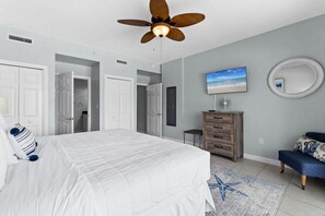 A bedroom with a bed, a ceiling fan, a TV, a dresser, and a bench.