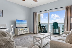 A living room with a television, a white cabinet, a coffee table, and a view of the sea through large sliding doors.