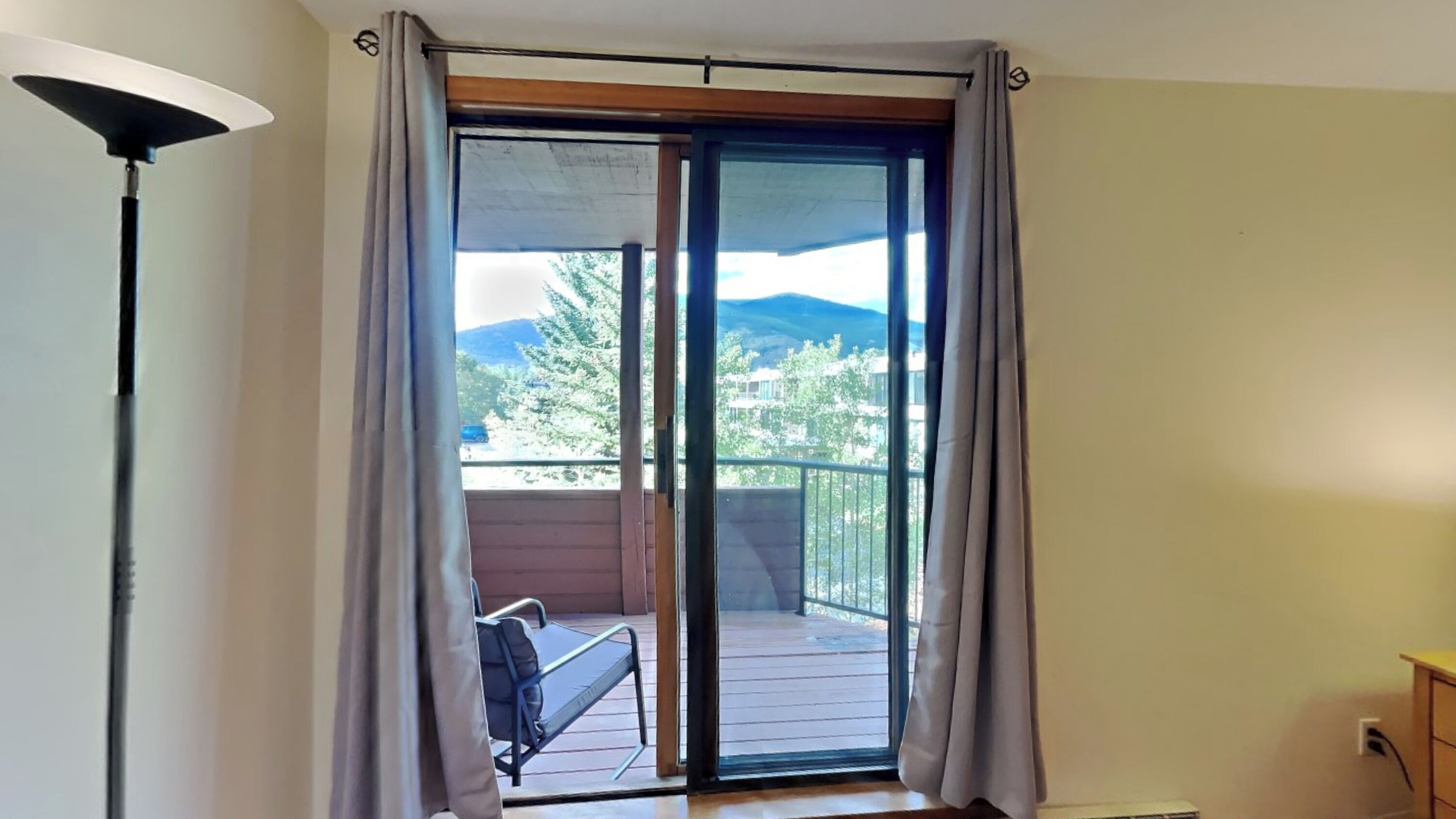 A room with a sliding glass door leading to a balcony with a view of trees and mountains.