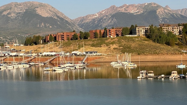Una marina con barche, un complesso di edifici a più piani e montagne sullo sfondo.