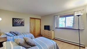 A bedroom with two beds, a television on a dresser, a window with curtains, and a poster on the wall. - Charming condo in the heart of Dillon, providing both comfort and harmony. (Dillon)