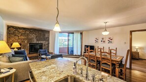 A living room with a stone wall, a fireplace, a television, and a dining area with wooden chairs and a table.