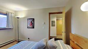 Un dormitori amb un llit, un cartell a la paret, una làmpada de peu i una porta que dona a una altra habitació.