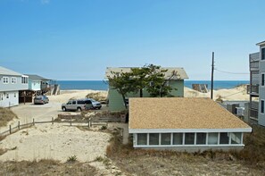 A beachfront property with a sandy driveway, a parked SUV, and a small building with a shingled roof.