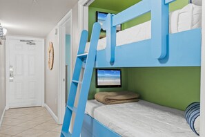 Une chambre avec un lit superposé, un téléviseur placé sur le lit du bas, une échelle et une porte ornée d’un motif circulaire sur le mur.