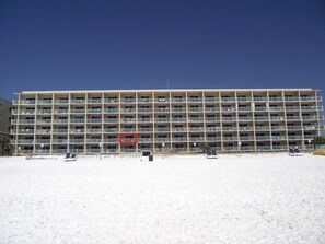 Un hôtel à plusieurs étages, doté de nombreux balcons, situé près d’une plage de sable.
