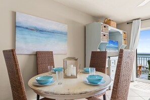 Un coin repas avec des chaises en osier, une table ronde, des bols bleus et un tableau encadré représentant un paysage marin.
