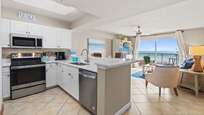 A modern kitchen with white cabinets, stainless steel appliances, and a view of the ocean.