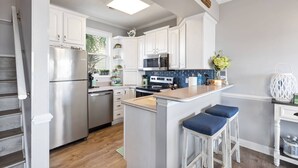 A kitchen with white cabinets, stainless steel appliances, a blue tiled backsplash, and a small island with stools. - Sweet Carolina - Perfect Surfside Oceanfront Location! (Surfside Beach)