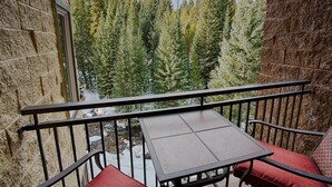 A balcony with a table and chairs, overlooking a forested area with a stream. - Walking distance to lifts/town! Underground parking! (Breckenridge)