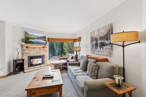 A living room with a stone fireplace, a sofa, a coffee table, and a floor lamp. - Walking distance to lifts/town! Underground parking! (Breckenridge)