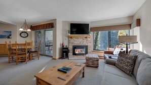 A living room with a fireplace, a sofa, a coffee table, and a dining area with chairs. - Walking distance to lifts/town! Underground parking! (Breckenridge)