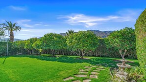 Un jardín bien cuidado con un sendero de piedra, césped verde exuberante y varios árboles.