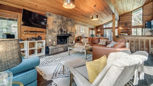 Un intérieur de chalet chaleureux avec une cheminée en pierre, un plafond en bois et de grandes fenêtres.