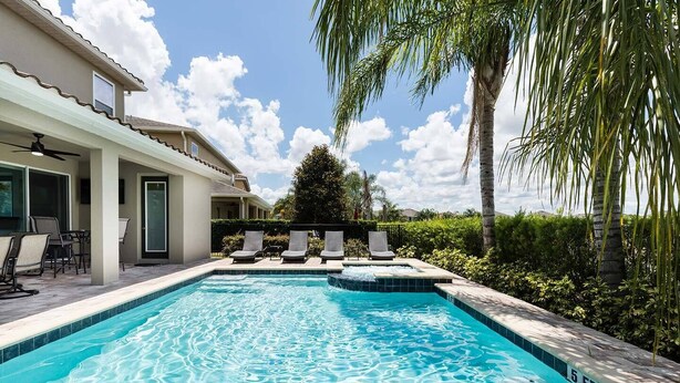 Une piscine avec des chaises longues, un patio couvert et une vue sur un immeuble d’habitation.