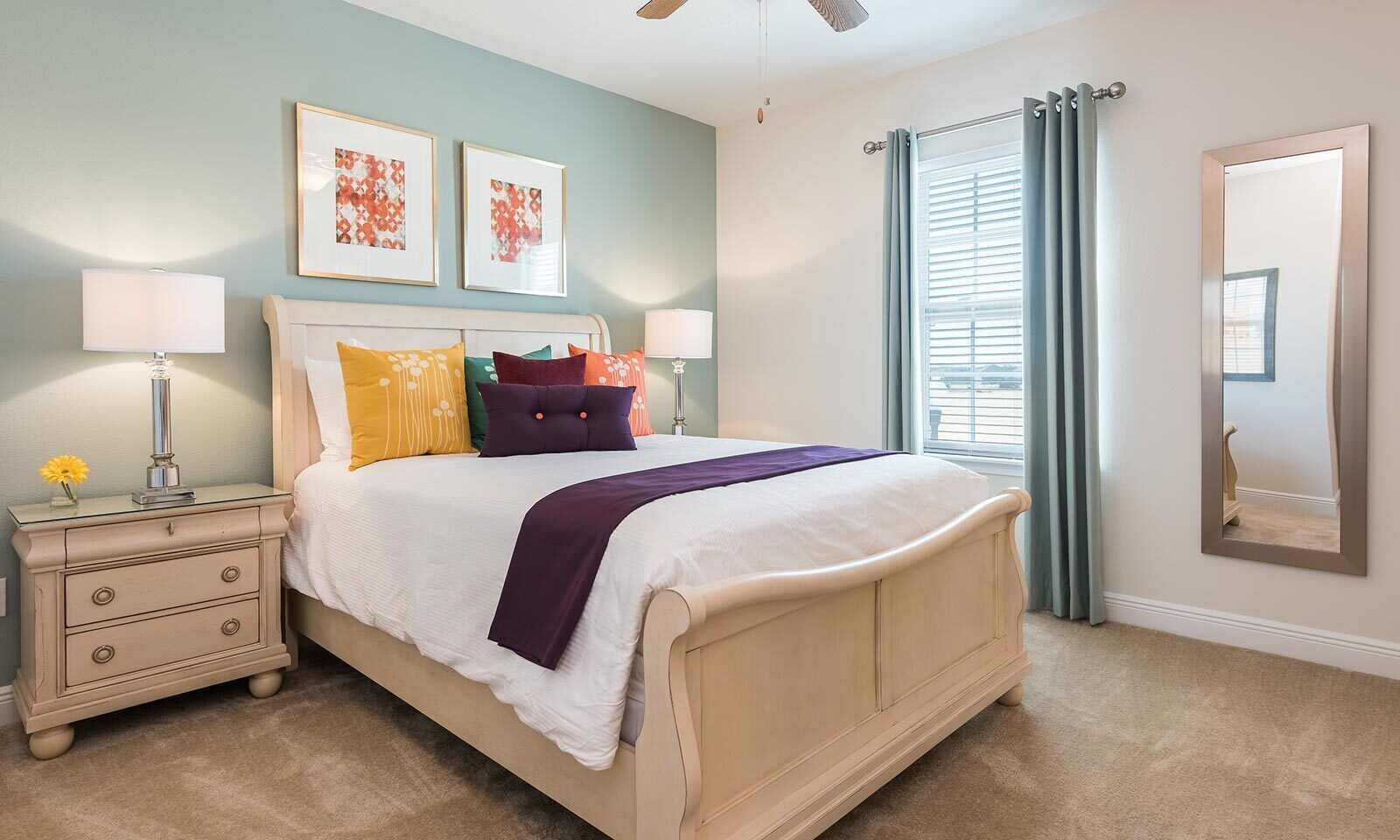 A bedroom with a bed, nightstands, a ceiling fan, a window with curtains, and framed artwork on the wall.