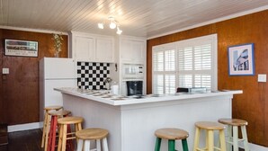 Una cocina con una isla central, armarios blancos, un salpicadero a cuadros y taburetes de madera.