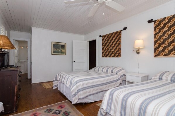 Una habitación con dos camas, ventilador de techo, lámpara, cómoda y una puerta.
