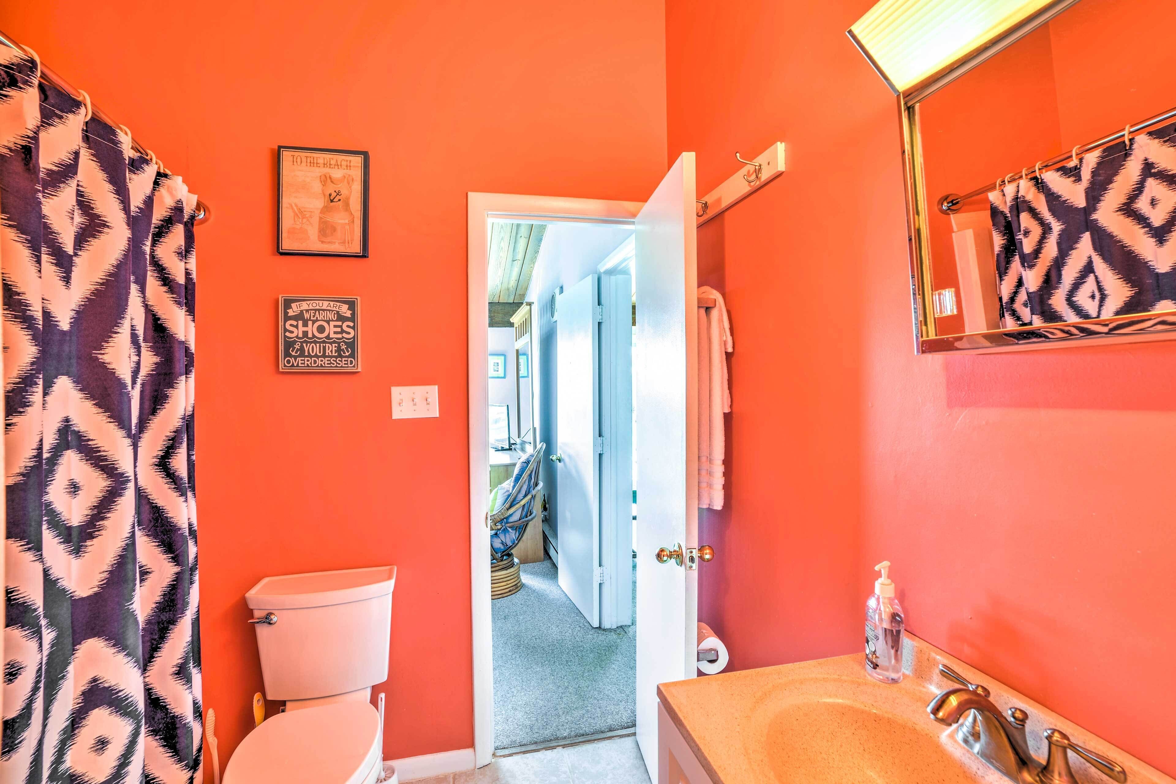 A bathroom with a toilet, sink, and shower curtain. There is a towel hanging on a rack and a sign on the wall.