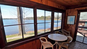 Puinen mökki, jossa on suuret ikkunat, joista avautuu näkymä järvelle, pyöreä pöytä tuoleineen ja seinällä oleva kartta.