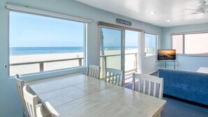 A room with a large window overlooking a beach, a wooden table, and a blue couch. - A magnificent view awaits you as you enter...this upper unit is one-of-a-kind! (Newport Beach)
