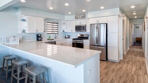 A modern kitchen with white cabinets, stainless steel appliances, a large island with stools, and a 'let's eat' sign. - A magnificent view awaits you as you enter...this upper unit is one-of-a-kind! (Newport Beach)