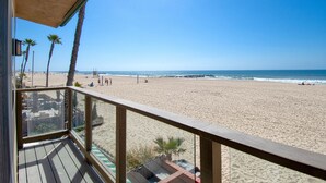 A beach view from a wooden deck with a railing, palm trees, and a lifeguard tower in the background. - A magnificent view awaits you as you enter...this upper unit is one-of-a-kind! (Newport Beach)