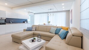 Un salon moderne avec un canapé d’angle beige, une table basse blanche et un coin cuisine en arrière-plan.
