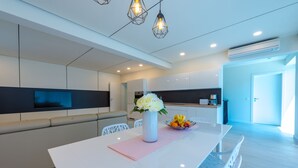 Une cuisine moderne avec des meubles blancs, un îlot central agrémenté d’un vase de fleurs et un coin salon avec des chaises blanches.