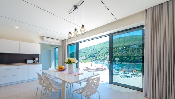 Une cuisine moderne avec des meubles blancs, une table à manger blanche et des chaises. Une grande fenêtre offre une vue sur un paysage verdoyant.