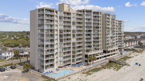 Een meerlaags hotel met balkons, een zwembad en uitzicht op het strand.