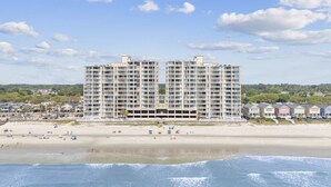 Een hotel aan het strand met meerdere verdiepingen, een strand op de voorgrond en een heldere lucht.